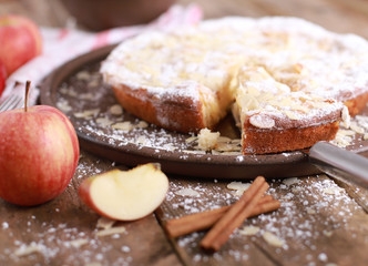 Sweet homemade apple pie on a plate with fresh apples and cinnamon sticks on a rustic wooden table