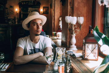 Attractive happy young man in a white stylish shirt sits on a chair near the window in a cozy cafe. Joyful handsome guy is resting