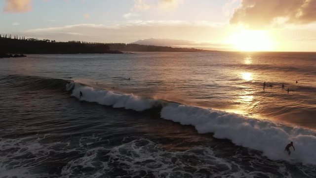 Surfers ride wave at sunset in Honokahua Bay, Hawaii, aerial