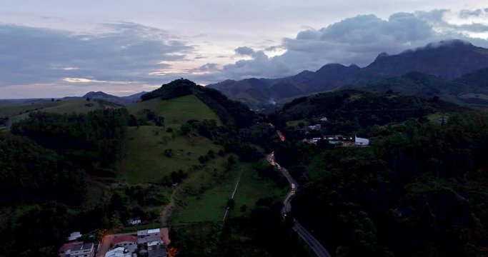 Drone image over the city of Cachoeiro de Itapemirim in Espirito Santo, southeast of Brazil. Small houses and forest below. In the highway some cars and trucks pass by.
