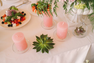 Coziness and style. Modern event design. Table setting at wedding reception. Floral compositions with beautiful flowers and greenery, candles, laying and plates on decorated table.