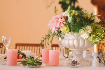Coziness and style. Modern event design. Table setting at wedding reception. Floral compositions with beautiful flowers and greenery, candles, laying and plates on decorated table.
