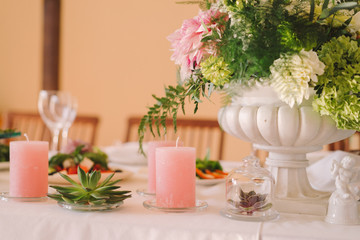 Obraz na płótnie Canvas Coziness and style. Modern event design. Table setting at wedding reception. Floral compositions with beautiful flowers and greenery, candles, laying and plates on decorated table.