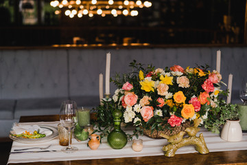 Coziness and style. Modern event design. Table setting at wedding reception. Floral compositions with beautiful flowers and greenery, candles, laying and plates on decorated table.