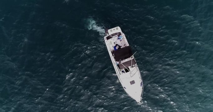 Drone zenital zoom out image of white boat sailing in the ocean. People walk around inside the boat. Video recorded in Espírito Santo, Southeastern Brazil.