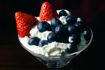 Berries strawberries and blueberries in whipped cream inside martini glass top view. 