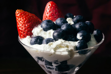 Berries strawberries and blueberries in whipped cream inside a martini glass. 