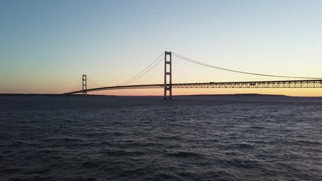 Wide aerial, cars drive over Mackinaw Bridge in Michigan at sunset