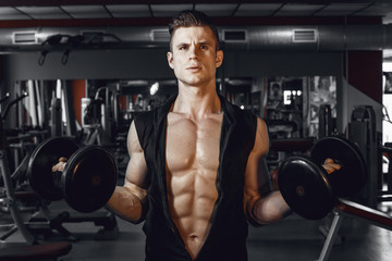 Muscular model sports young man exercising in gym with dumbbell. Portrait of sporty healthy strong muscle. Fitness trainer. Sport workout bodybuilding motivation concept. Sexy torso.