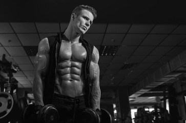 Fototapeta na wymiar Muscular model sports young man exercising in gym with dumbbell. Black and white portrait of strong muscle. Fitness trainer. Sport workout bodybuilding motivation concept. Sexy torso.