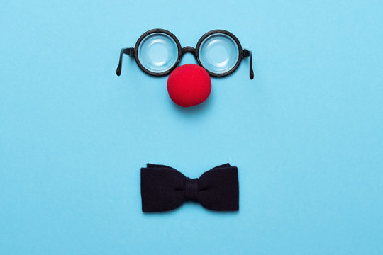 Funny glasses, red clown nose and tie lie on a colored background, like a face.