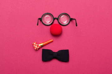 Funny glasses, red clown nose and tie lie on a colored background, like a face.