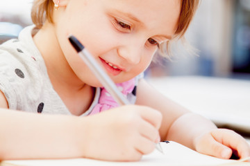 Funny portrait happy cute child girl laughing and writing a letter. Positive emotion, education and happy childhood concept.