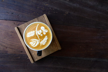 Top view a cup of hot coffee cappuccino with cute signature rabbit, flower and leaf latte art pattern in black ceramic cup on rough wooden tray and table. 