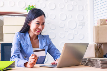 Young  Asia Businesswoman use laptop. She is use laptop for order online and show credit cards. She  is smile and happy.E-commerce , Shopping , Photo concept work and Business.