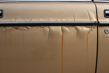 Close-up a gold old car door with crack and scratch colour skin. A vintage sedan car left unattended on street with ripped off and peeled skin cracked pattern found all over. Selective focus.