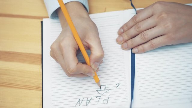 Close-up of female hand writing down strategy in notebook with pencil. Businesswoman making up new business plan. Strategy and planning concept