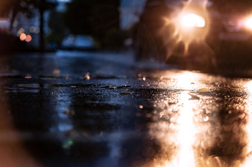 Night road blurred. Headlight of car in the dark while heavy raining. Rain in the city. Road, pavement, close up. Water splashes, spills on roadway