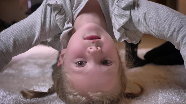 Close-up upside down portrait of small caucasian girl making a bridge and showing funny faces into camera.