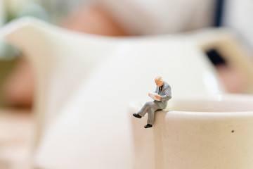 Miniature people : businessman reading a book on a cup of tea