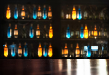 top of wood table with neon orange blue light of alcohol bottle in dark bar and club background