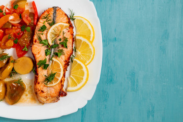 Baked salmon fillet medallion with salad of pickled vegetables and mushrooms on a white plate on a blue background, top view, flatlay, place for text, copy space