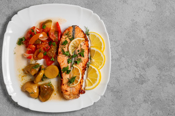 Baked salmon fillet medallion with salad of pickled vegetables and mushrooms on a white plate on a gray background, top view, flatlay, place for text, copy space