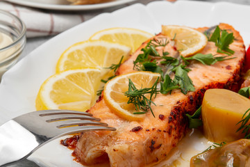 Baked salmon fillet medallion with salad of pickled vegetables and mushrooms on a white plate on a gray background, close up