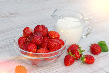 Fresh ripe strawberries in a bowl and iogurt on a white table outdoors on a summer day
