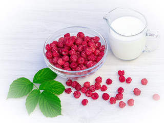 Fresh raspberries in a glass bowl and natural iogurt on a white wooden table. Healthy eating concept