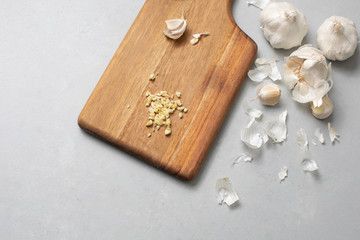 Fototapeta na wymiar Minced Garlic on Wooden Cutting Board with Garlic Cloves and Bulbs in Background on Gray Countertop