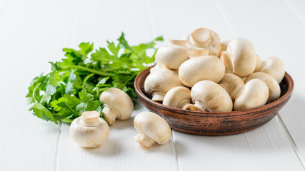 Fresh mushrooms in a clay bowl with parsley leaves on a white wooden table. Vegetarian cuisine.
