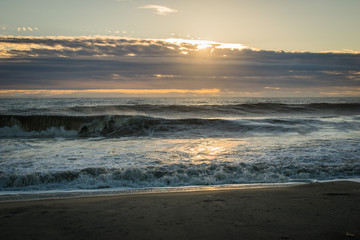 Fototapeta na wymiar Waves Breaking on the Sandy Shore at Sunrise