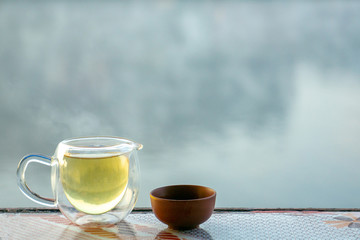Teapots and teacups placed on the table have a view behind the lake with fog floating over the surface.