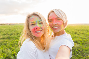 Indian festival of holi, people concept - two young woman taking selfie with colourful powder on the faces