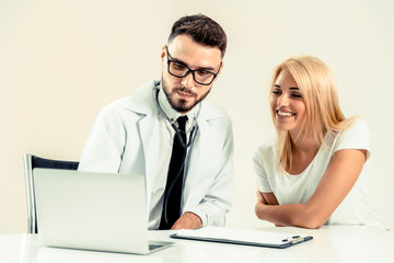 Male doctor talks to female patient in hospital office while looking at the patients health data on...