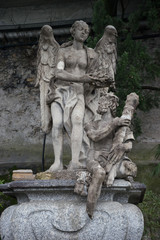 Fototapeta na wymiar Italy, Varenna, Lake ComoVarenna, Italy - March 31, 2018: Stone Sculpture artifact at gardens of Villa Monastero, a person sitting on a rock