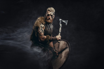 Medieval warrior berserk Viking with tattoo and in skin with axes attacks enemy. Concept historical photo - obrazy, fototapety, plakaty