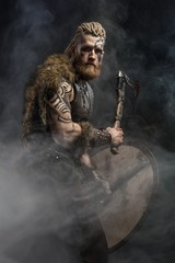 Medieval warrior berserk Viking with tattoo and in skin with axes attacks enemy. Concept historical...