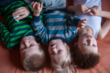 Three happy blond boys ate lots of candy. Children's tongue turned blue from marmalade. Striped home pajamas, proton purple background, sofa. Children have good time together.