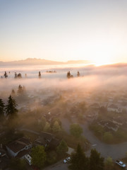 Aerial view of a residential neighborhood covered in a layer of fog during a vibrant sunrise. Taken in Greater Vancouver, BC, Canada.