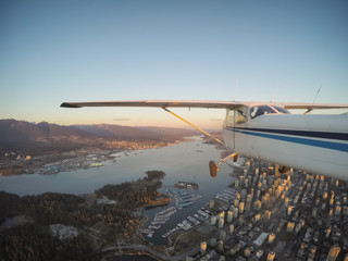 Small airplane flying over Downtown City during a vibrant sunset. Taken in Vancouver, British Columbia, Canada.