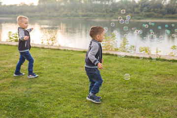 Children and nature concept - Little Brothers trying to catch soap bubbles