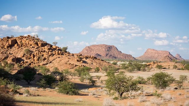 rolling cumulus clouds pass over dry rocky savannah landscape in namibia and shadows creep into frame as the sun begins to set