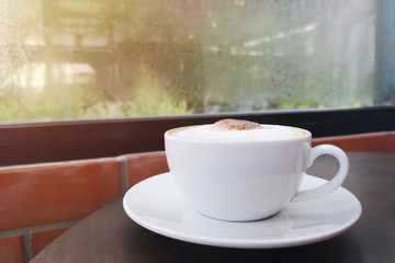Cappuccino served hot. drink made from white coffee cup on the wooden table  beside the window. morning atmosphere in room brick wall style.