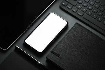 Office stationery with blank screen mobile smart phone on dark background.