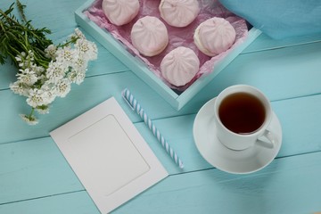 Spring tea.Flat lay.Spring to-do list.pink marshmallow and blank notebook, cup of tea and white flowers on a blue wooden board background.top view, copy space.Spring mood