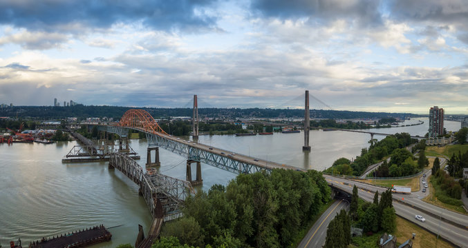 Aerial panoramic view of Pattullo and Skytrain Bridge going across Fraser River duing a cloudy evening before sunset. Taken in New Westminster, Vancouver, BC, Canada.