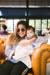 Portrait of young mother and her newborn baby sitting on sofa  in a nice cafe, Happy childhood, a...