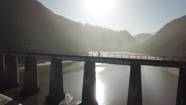 Drone video of man walking accross a giant bridge at sunset. The bridge is over a river mouth and its sunset.